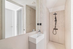 Interior of modern bathroom with beige tiles, shower and small sink.